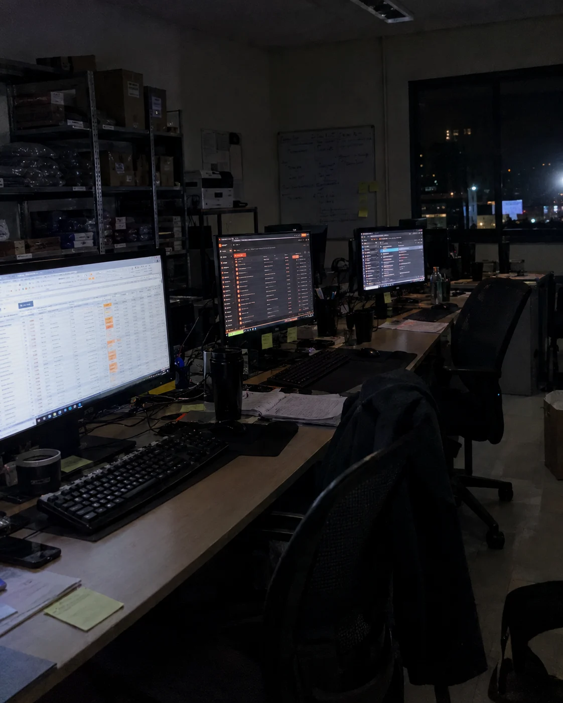 Escritório vazio à noite, com as luzes apagadas e as telas dos computadores acesas